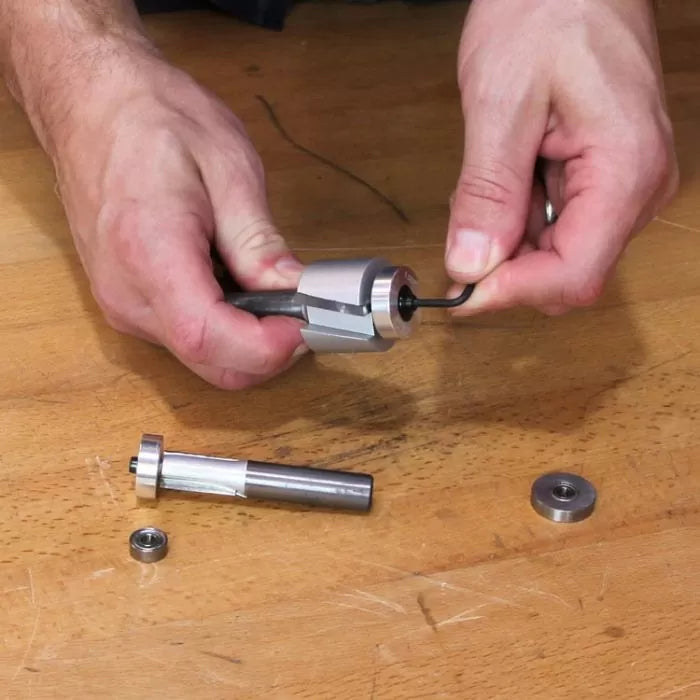 Hands assembling a woodworking router bit with hex key and bearings on a workbench