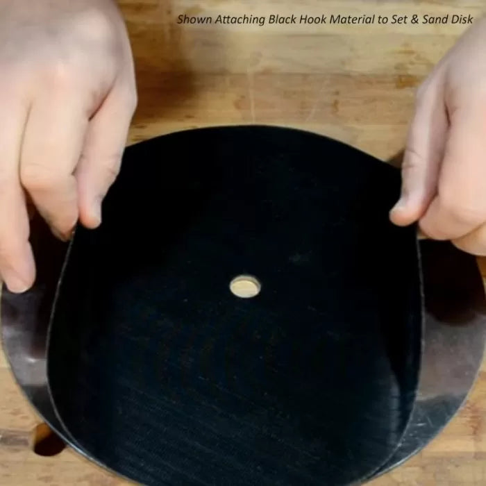 Attaching black hook material to sanding disk on wood workbench for woodworking tools