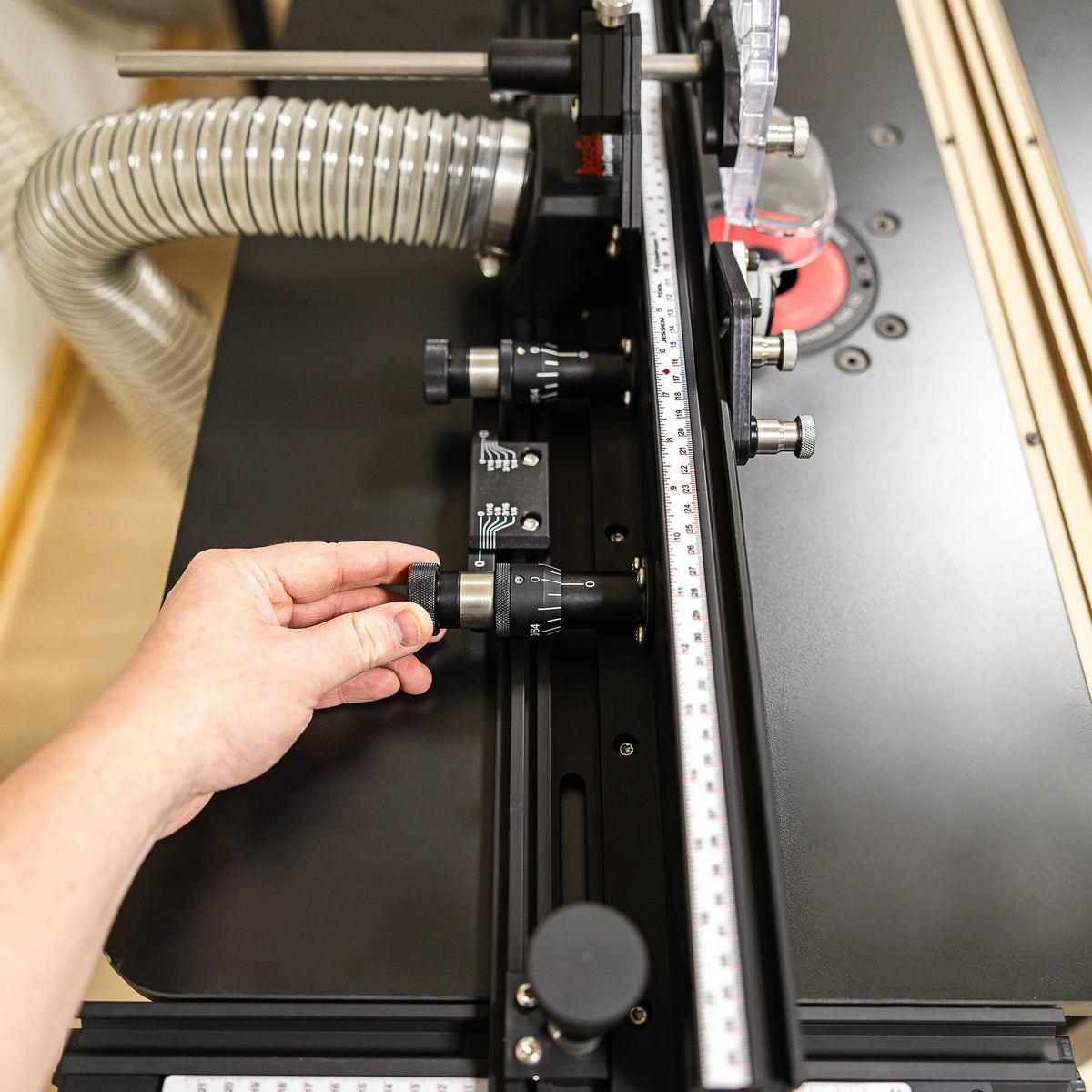 Hand adjusting micro dial on precision router table fence with dust collection hose attached