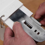 Hands using a jig to align and sharpen a woodworking plane blade on a workbench.