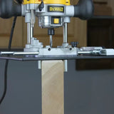 Plunge router with edge guide cutting a square wood post in a woodworking workshop.
