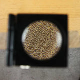 Magnified wood grain pattern viewed through a loupe on a light work surface