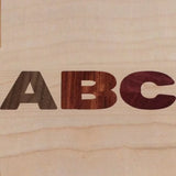 Wood inlay letters A, B, and C on a light wood surface, showcasing woodworking precision.
