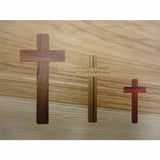 Three wooden cross inlays in different sizes and wood tones on a light wood background