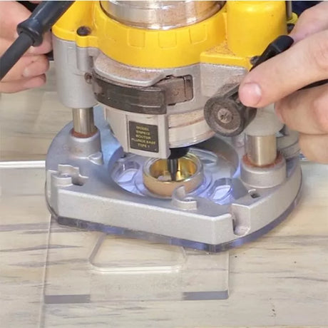 Handheld woodworking router with guide bushing in use on clear base plate