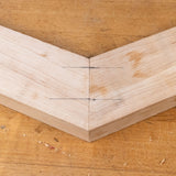 Close-up of a miter joint with dowel alignment marks on light wood, resting on a workbench