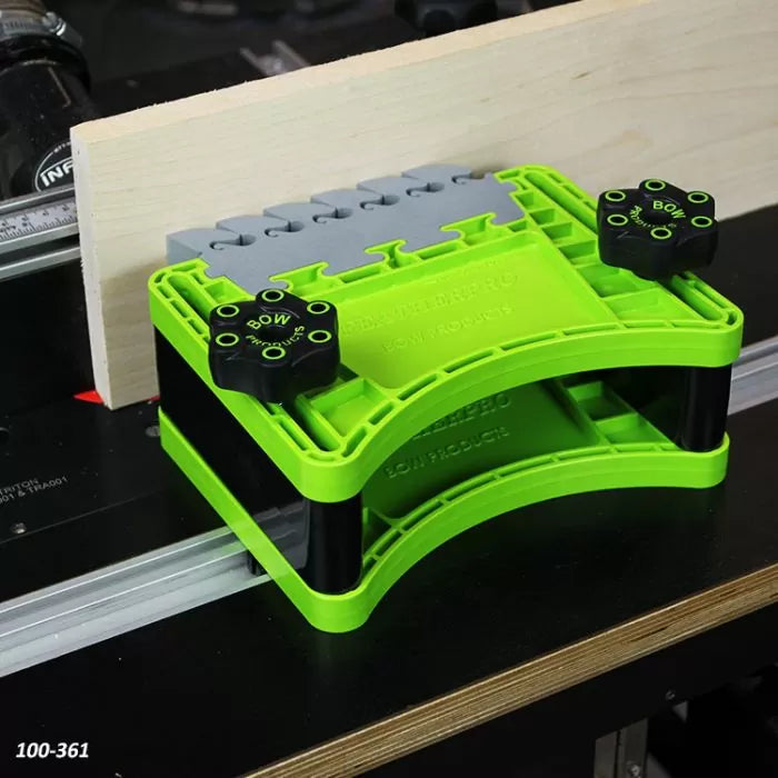 Green woodworking featherboard tool securing wood on a router table for safe cutting