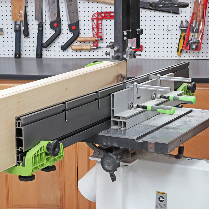 Band saw fence system with green clamps holding wood, woodworking tools in background