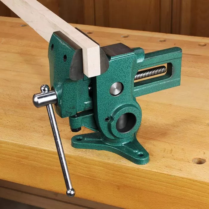 Green woodworking vise mounted on a workbench holding a wooden board