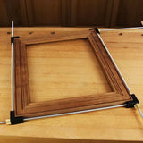 Woodworking picture frame held by corner clamps and steel rods on a workbench