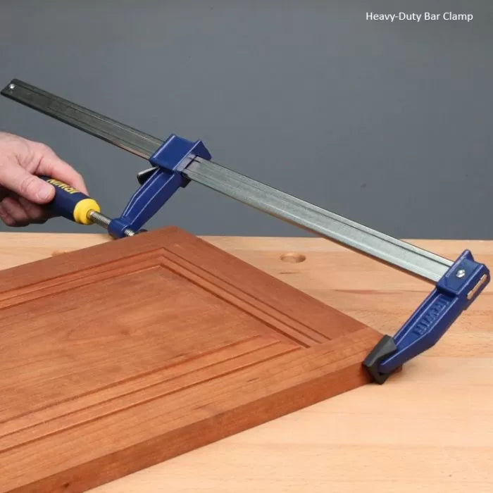 Heavy-duty bar clamp securing wooden cabinet door on workbench for woodworking