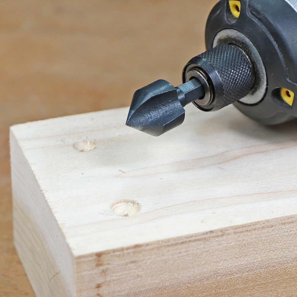 Countersink drill bit attached to power drill beside pre-drilled holes in wood block