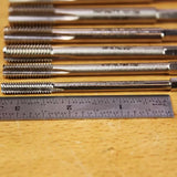 Metal thread taps aligned on workbench with steel ruler for woodworking tool measurement