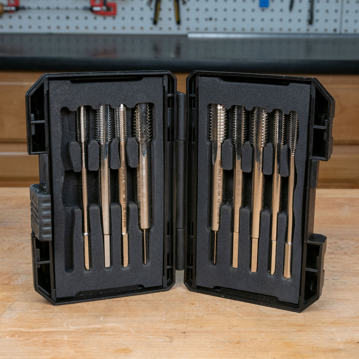 Thread tap set with metal taps in a black protective case on a woodworking bench.