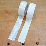 Two rolls of double-sided woodworking tape unspooled on a wood workbench.