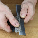 Sharpening a woodworking chisel with a diamond honing tool on a wooden workbench