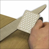Hand sharpening a knife blade with a DC300 diamond sharpening card on wood surface