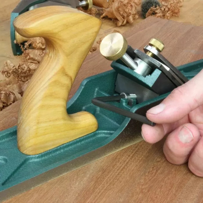 Hand adjusting a woodworking hand plane tool on a wooden workbench with wood shavings