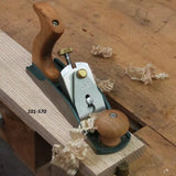 Bench hand plane smoothing wooden board with wood shavings on workbench