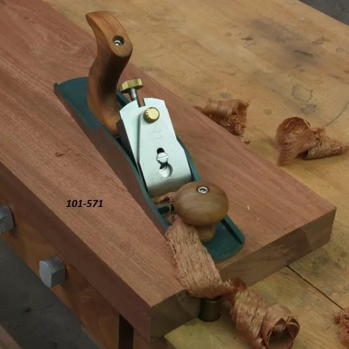 Hand plane woodworking tool smoothing a wood board on a workbench, labeled 101-571.