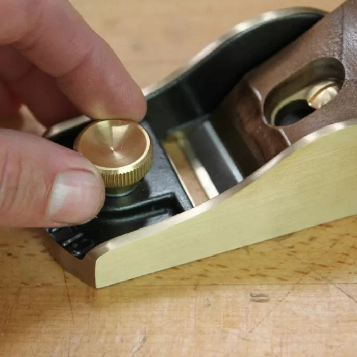 Hand adjusting brass knob on woodworking hand plane tool on a workbench