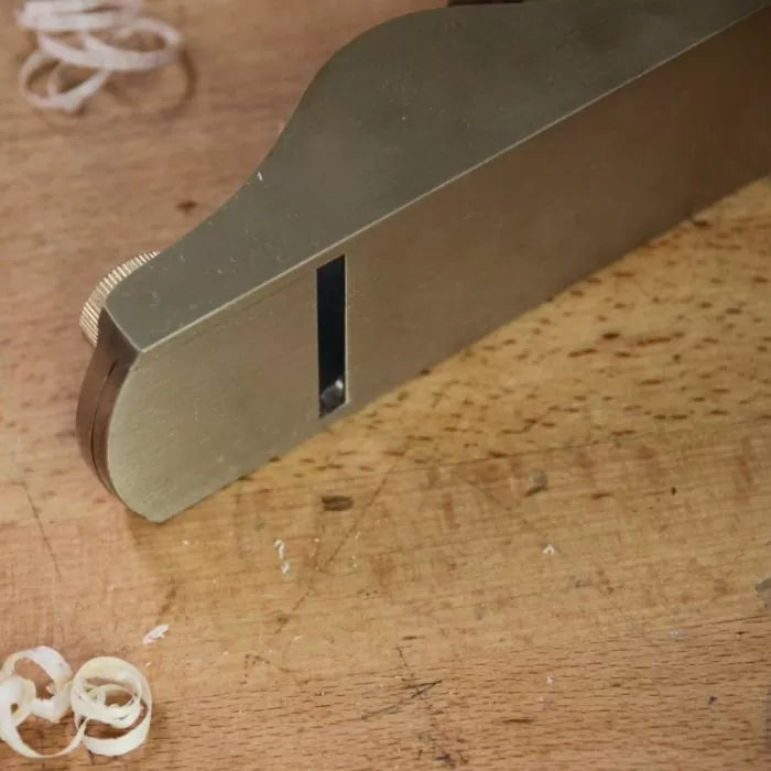 Brass woodworking hand plane on a workbench with wood shavings, precision tool detail