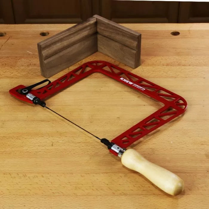 Red coping saw with wooden handle on workbench, wood corner molding in background