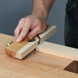 Hand using a wooden shoulder plane to trim a wood tenon on a workbench