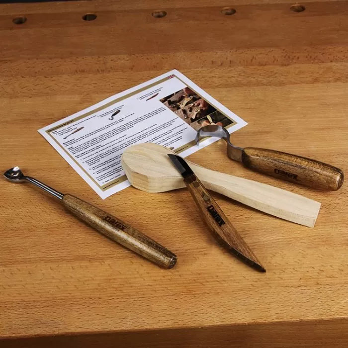 Wood carving tools set with spoon blank and instructions on a wooden workbench