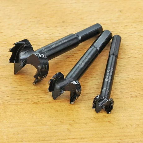 Three black forstner drill bits for woodworking on a wooden surface