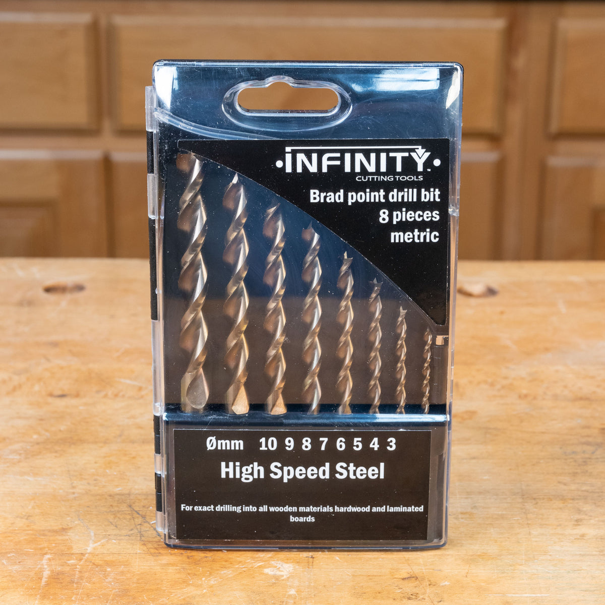 Metric brad point drill bit set, 8 pieces, high speed steel in packaging on wooden workbench.