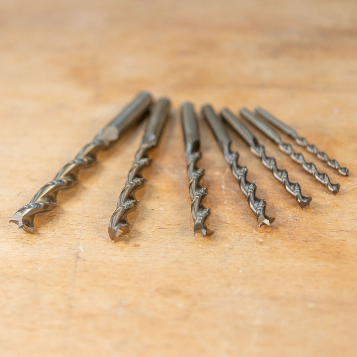 Set of seven woodworking drill bits with sharp tips on a wooden workbench