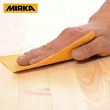 Hand sanding wood surface with yellow sandpaper, Mirka logo visible in corner