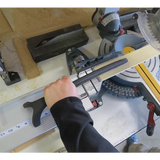 Woodworker using stick push block to guide wood safely on miter saw in workshop