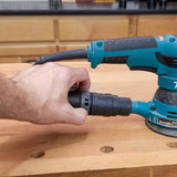 Hand attaching dust hose to orbital sander on woodworking bench, workshop background