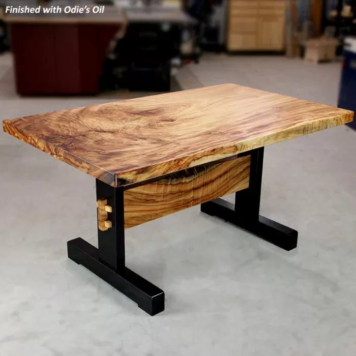 Live edge hardwood table with black metal legs in a woodworking shop setting