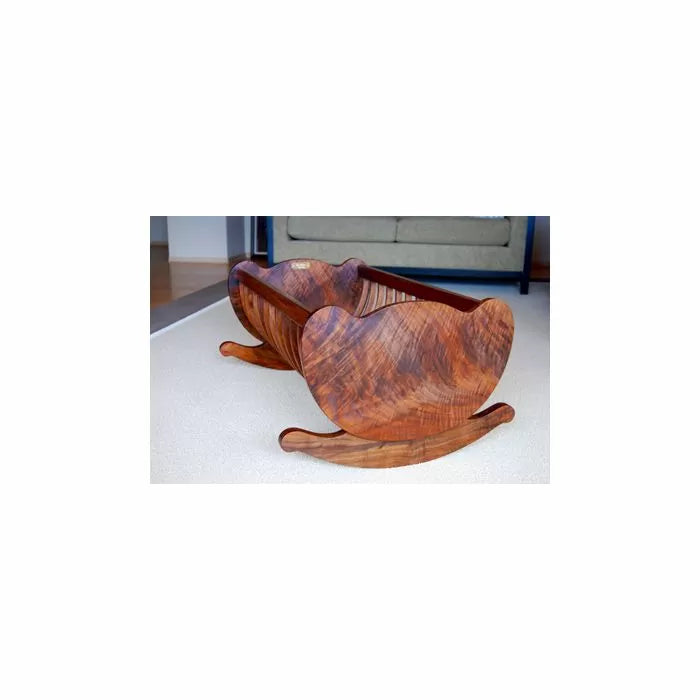 Wooden rocking cradle with decorative curves on a carpeted floor, handmade woodworking project