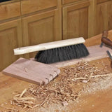 Woodworking bench brush with black bristles cleaning wood shavings on a workbench