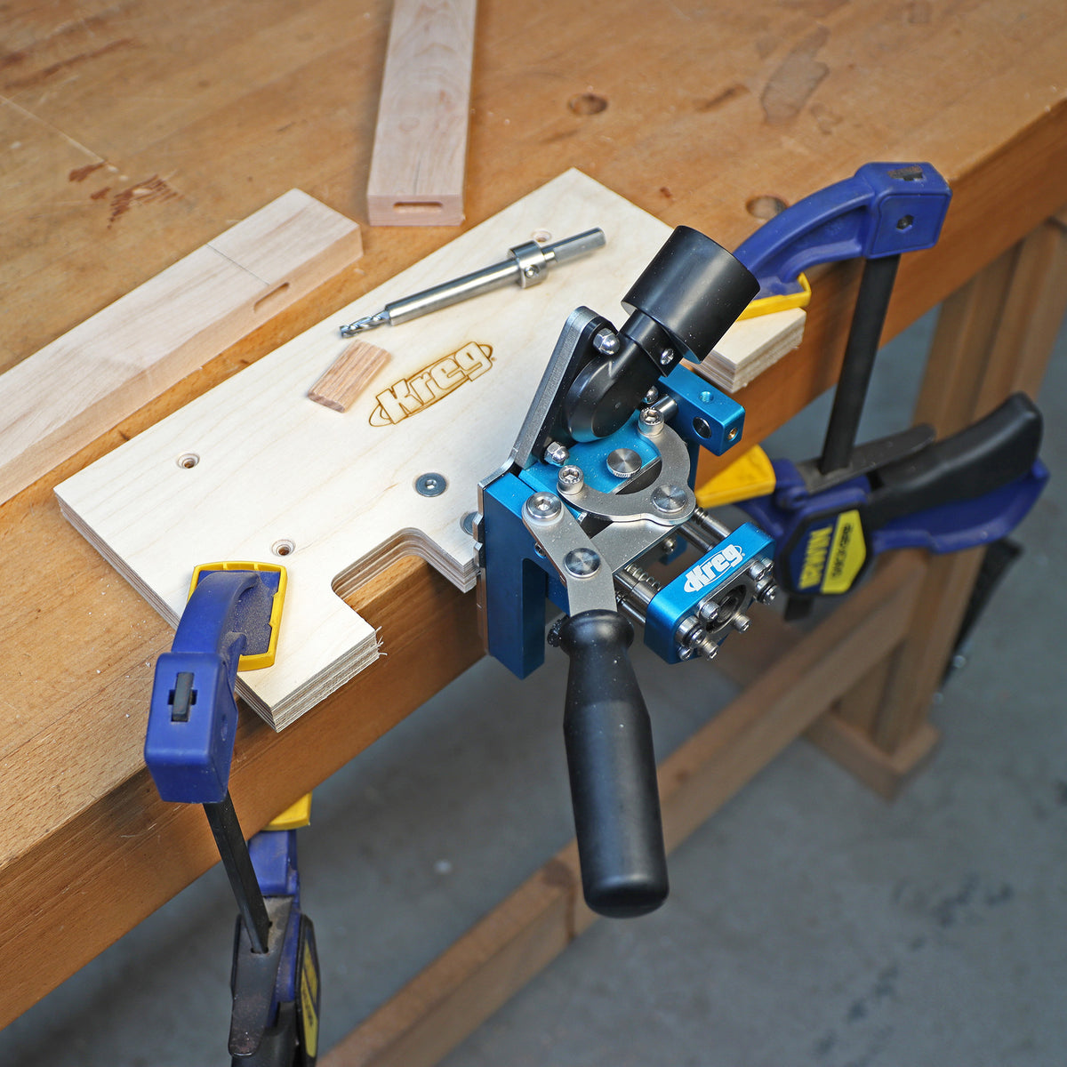 Woodworking mortise jig clamped to workbench with handle, drill bit, and wood pieces