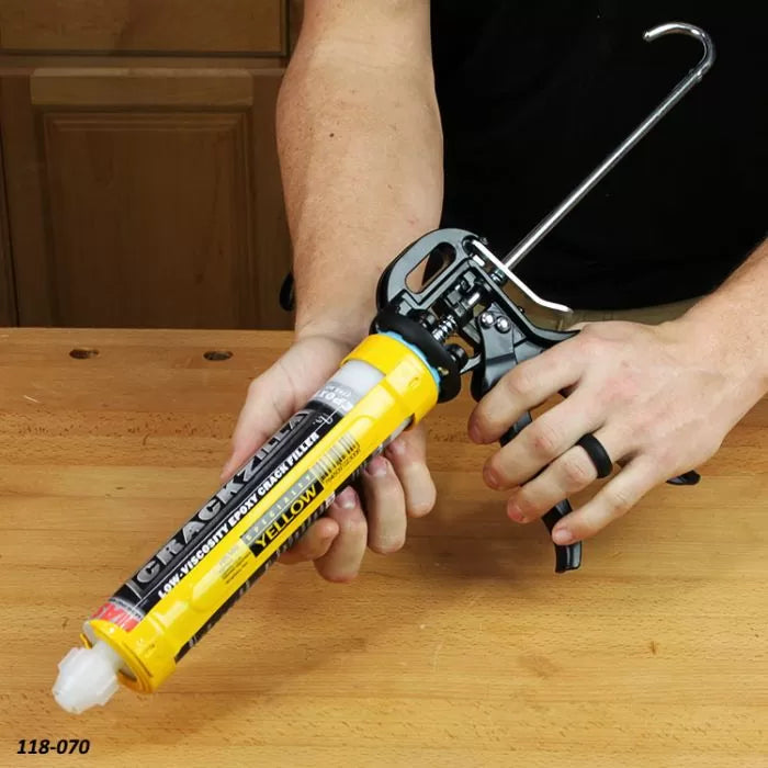 Person using a yellow caulking gun on a woodworking bench, applying adhesive sealant