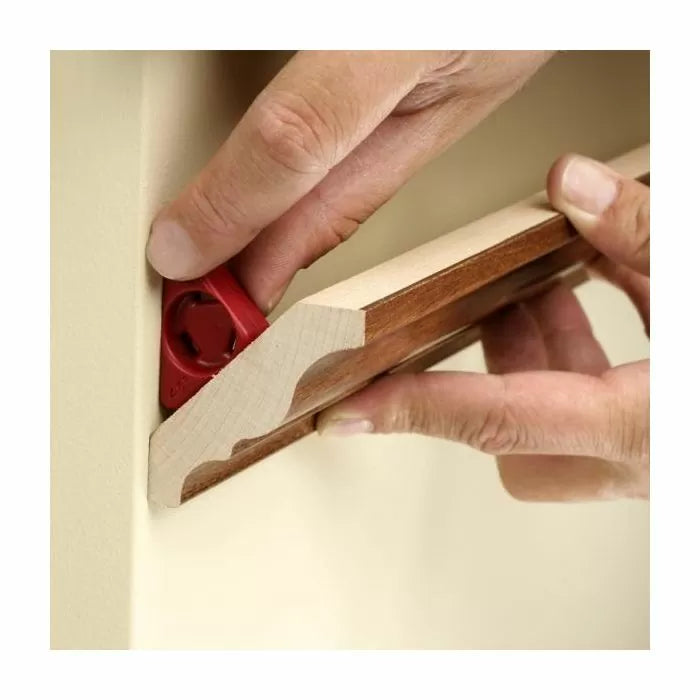 Hands using a red gauge tool to align wooden crown molding against a wall