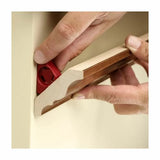 Hands using a red gauge tool to align wooden crown molding against a wall