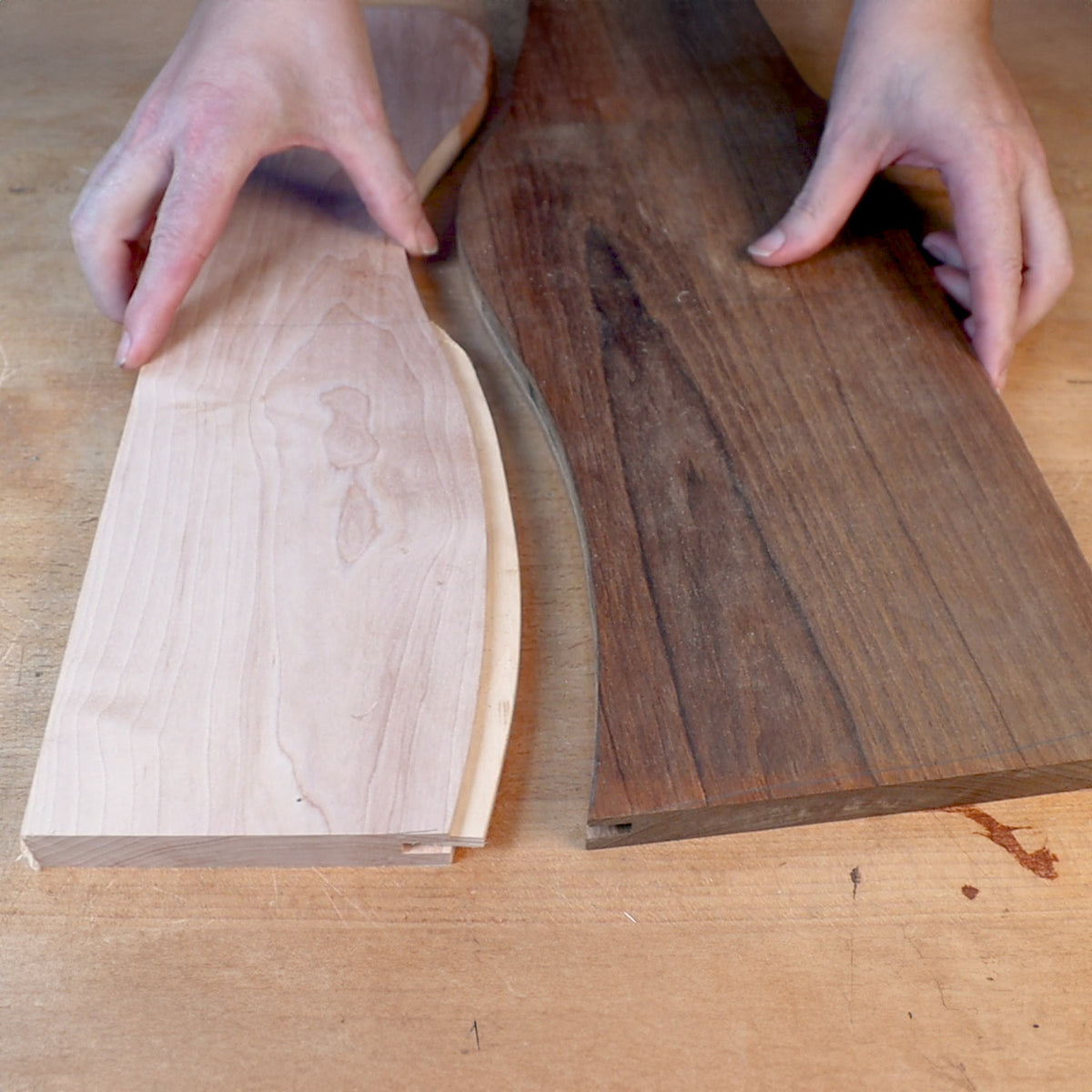 Hands holding two curved wood boards with smooth edges on a woodworking bench