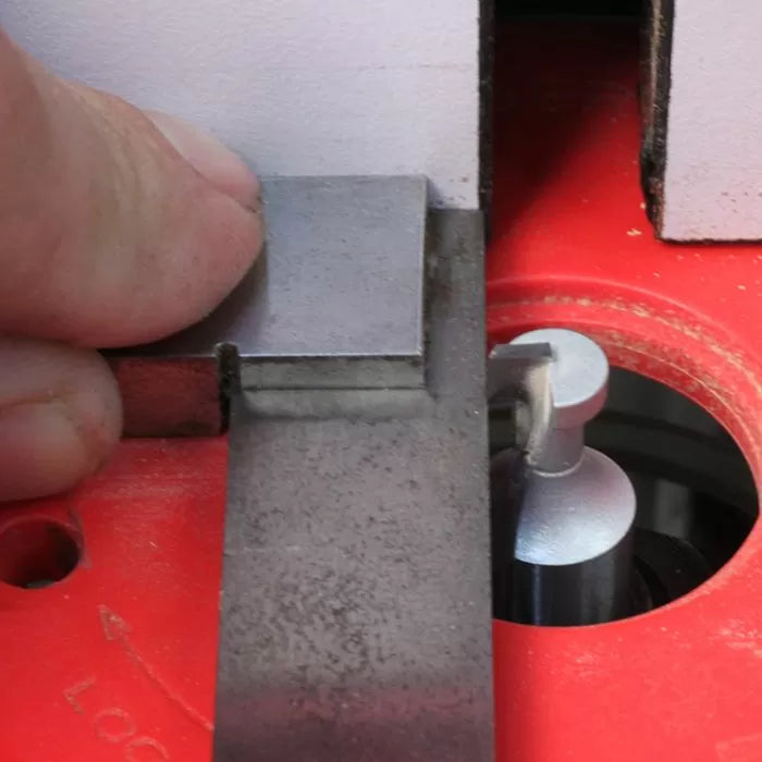 Close-up of a woodworking router bit setup with alignment tool on red router table.