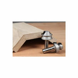 Two woodworking router bits next to a shaped wooden board on a workbench
