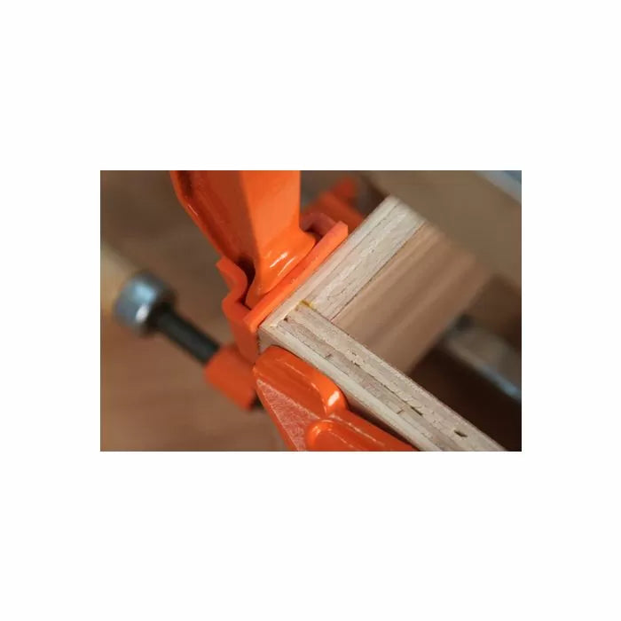 Wood glue-up with orange woodworking clamps securing a mitered joint on a workbench