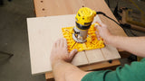 Woodworker using a handheld router with a yellow guide on a wooden board for precise grooving.