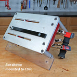 Woodworking clamping fixture with metal bar and red handles mounted on workbench.