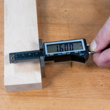 Digital marking gauge measuring wooden board thickness on a workbench