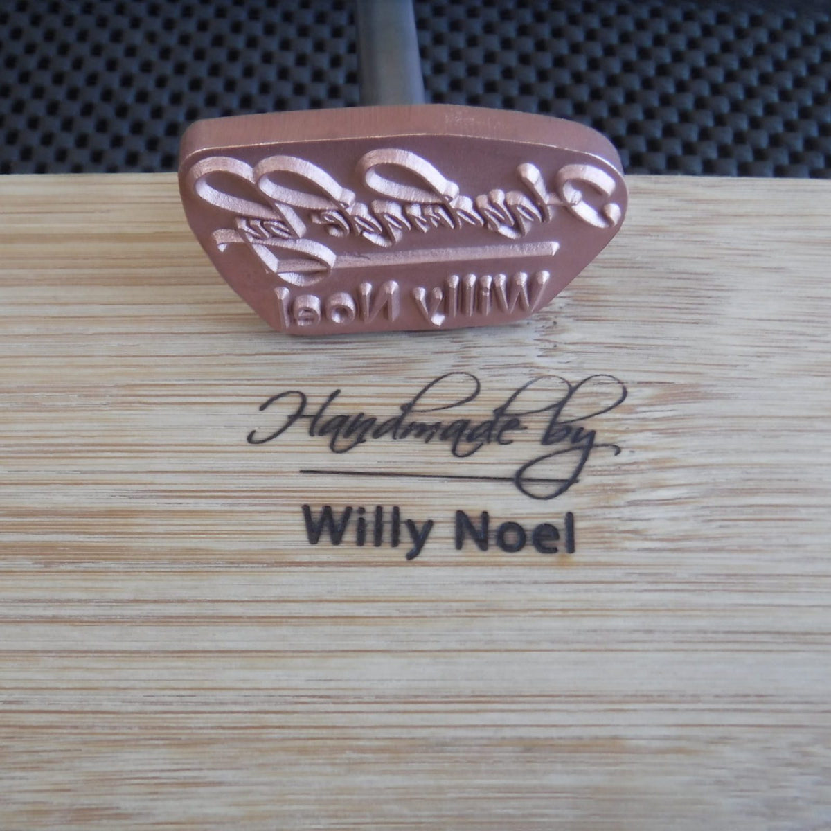 Custom wood branding iron marking 'Handmade by Willy Noel' on a wooden surface